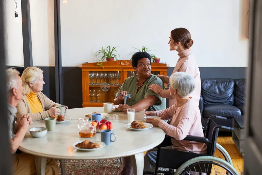 A woman in a wheelchair is actively participating in a discussion with people gathered around a table, promoting inclusivity.