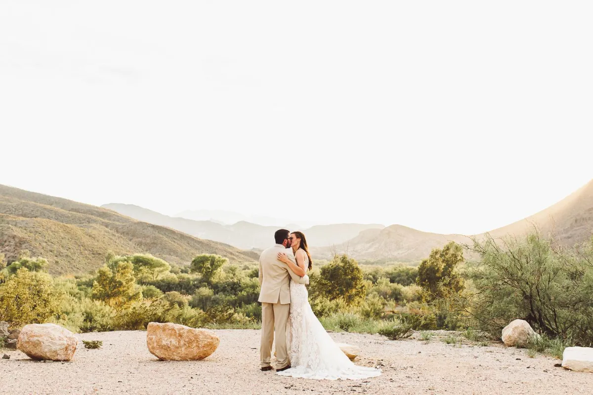 Bride and groom kissing with a mountain backdrop in Lajitas Golf Resort Terlingua, TX, photographed by Double Knot Photography, showcasing an intimate wedding moment in nature.
