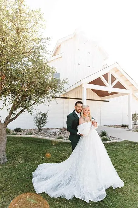 Bride and groom posing in front of the white barn at Sabrina Cedars in Abilene Texas, photographed by Double Knot Photography, with a rustic and romantic wedding vibe.