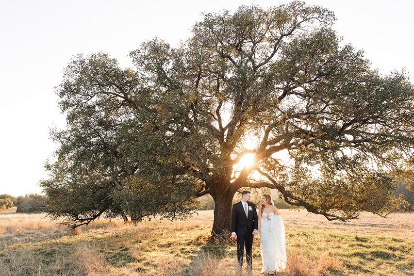 Bride and groom under an oak tree at sunset, captured by Double Knot Photography, with warm golden light creating a romantic wedding scene at Sparrow Creek Ranch in Graham Texas.