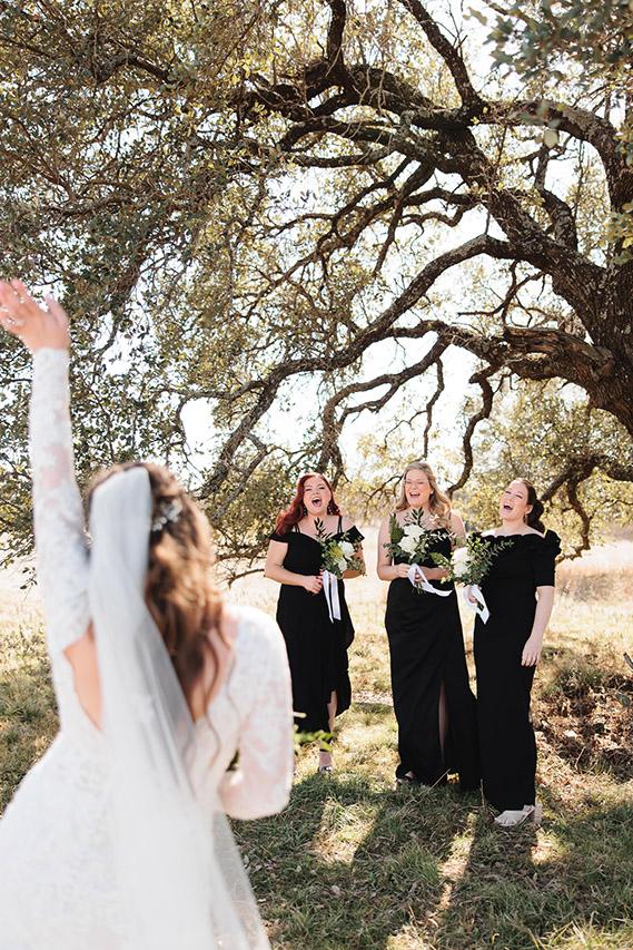 Bride and bridesmaids laughing under an oak tree, captured by Double Knot Photography, showcasing a joyful wedding party moment at Sparrow Creek Ranch in Graham Texas