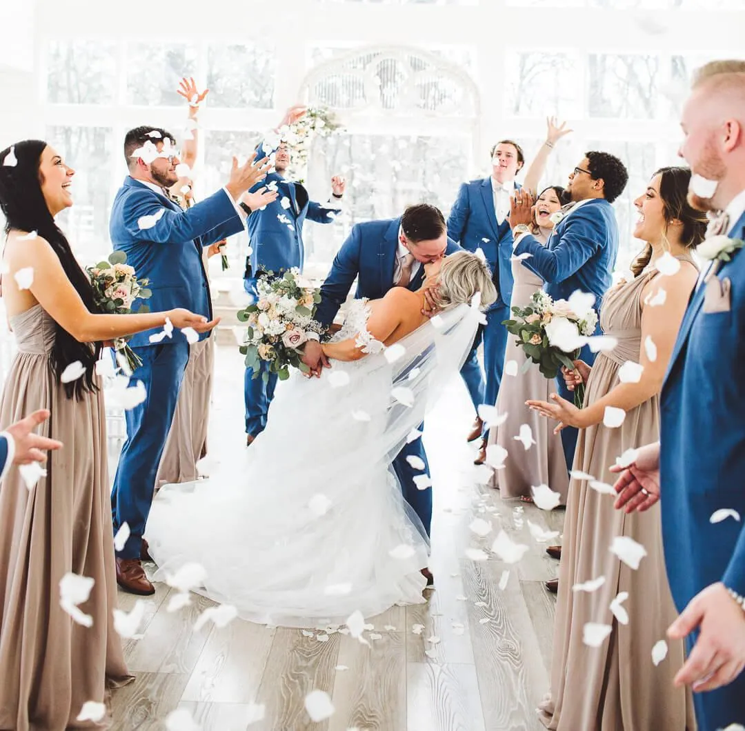 Wedding party tossing petals at the French Farmhouse chapel as the bride and groom kiss, captured by Double Knot Photography, highlighting a joyful celebration.