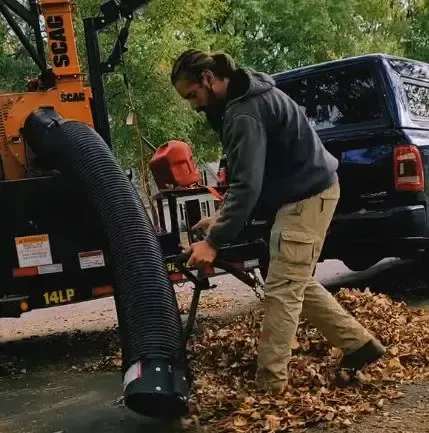 Worker vacuuming fallen leaves into collection unit for fall cleanup by Apple Valley Lawn and Snow