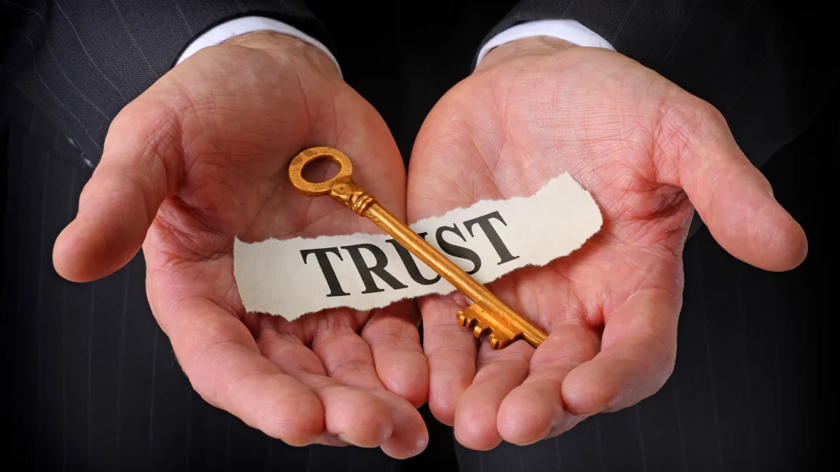 Close-up of a person holding a golden key labeled “TRUST,” symbolizing security and protection of family assets through a living trust.