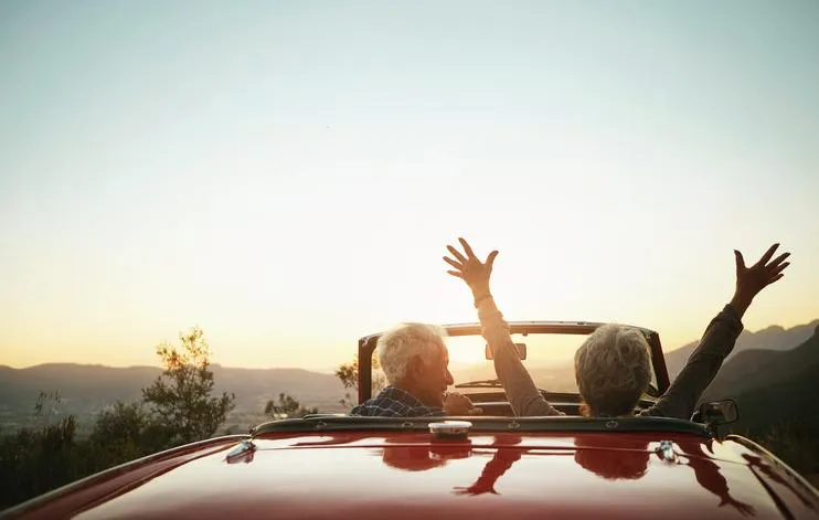 a retired couple driving into the beautiful sunset in a convertible