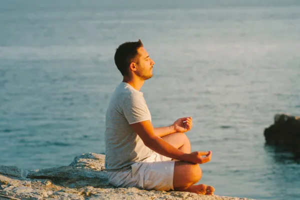 Person sitting by a calm lake at sunset, meditating and reflecting emotional mastery and balance