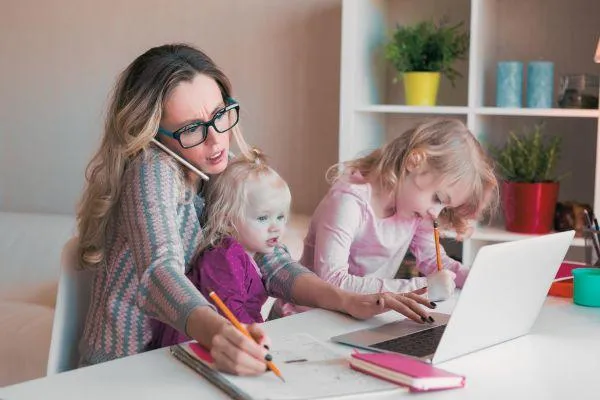 Mom juggling work with a baby and toddler looking stressed and overwhelmed