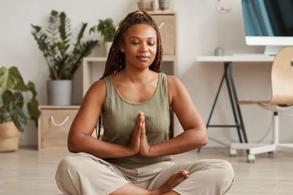 Woman doing yoga pose on floor with computer in the background