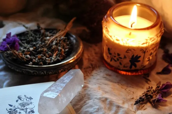 Candle in a jar with a bowl of lavender and a clear quartz crystal on top of a notebook
