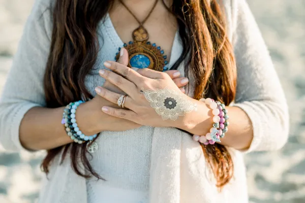 A woman dressed in white with long brown hair holding both hands to her heart.  She is wearing a long turquoise necklace and a turquoise bracelet and ring