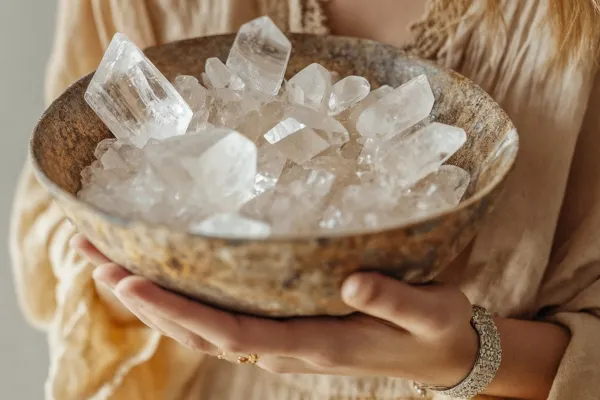Hands cradling wooden bowl of clear quartz crystals in warm, natural setting.
