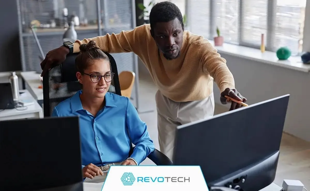 Two office colleagues at a desk looking at a computer monitor troubleshooting an IT issue.