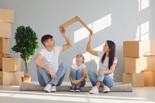 family sitting on the floor, parents holding cardboard roof over child's head