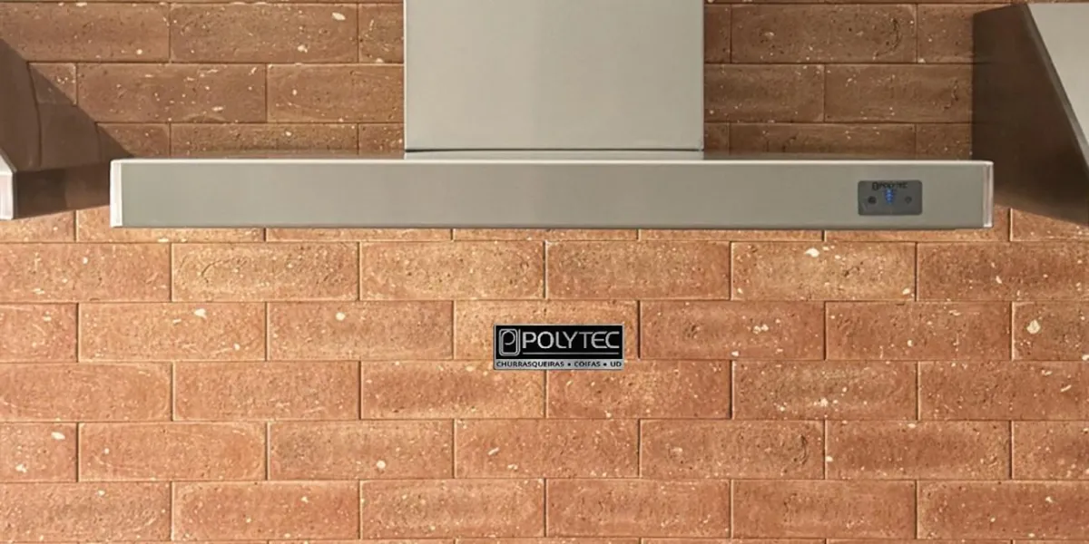 Coifa de parede inox Polytec instalada em cozinha com parede de tijolos, ideal para eliminar odores e gordura durante o preparo de alimentos