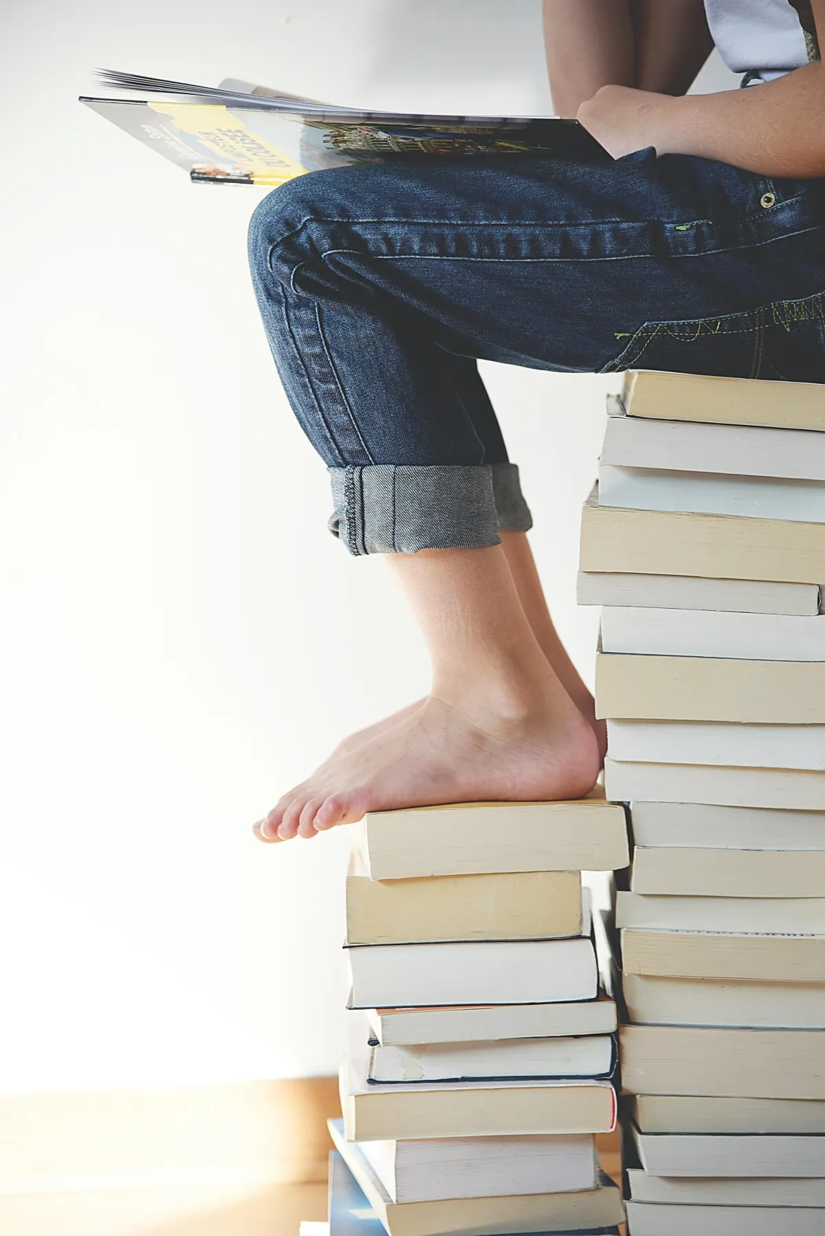 Legs wearing jeans and barefoot sitting on a stack of books
