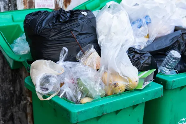 Green garbage bin overflowing with plastic bags, bottles, and household waste. 