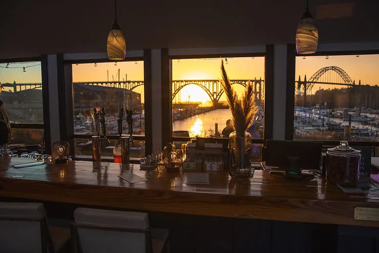 Outdoor seating at Rogue Spirits Sunset Bar in Newport, Oregon, overlooking Yaquina Bay Marina, offering handcrafted cocktails, Rogue ales, and coastal views.