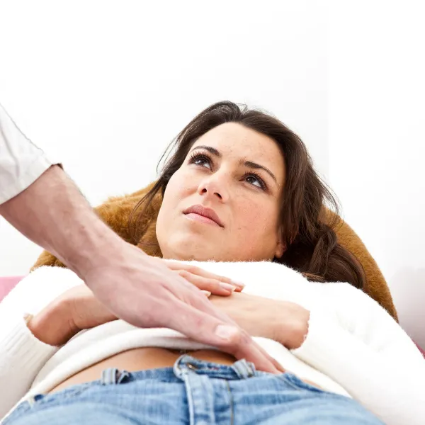 Female patient undergoing a pelvic floor assessment with a healthcare provider. The provider is palpating the abdominal region to assess the muscles and connective tissues of the pelvic floor.