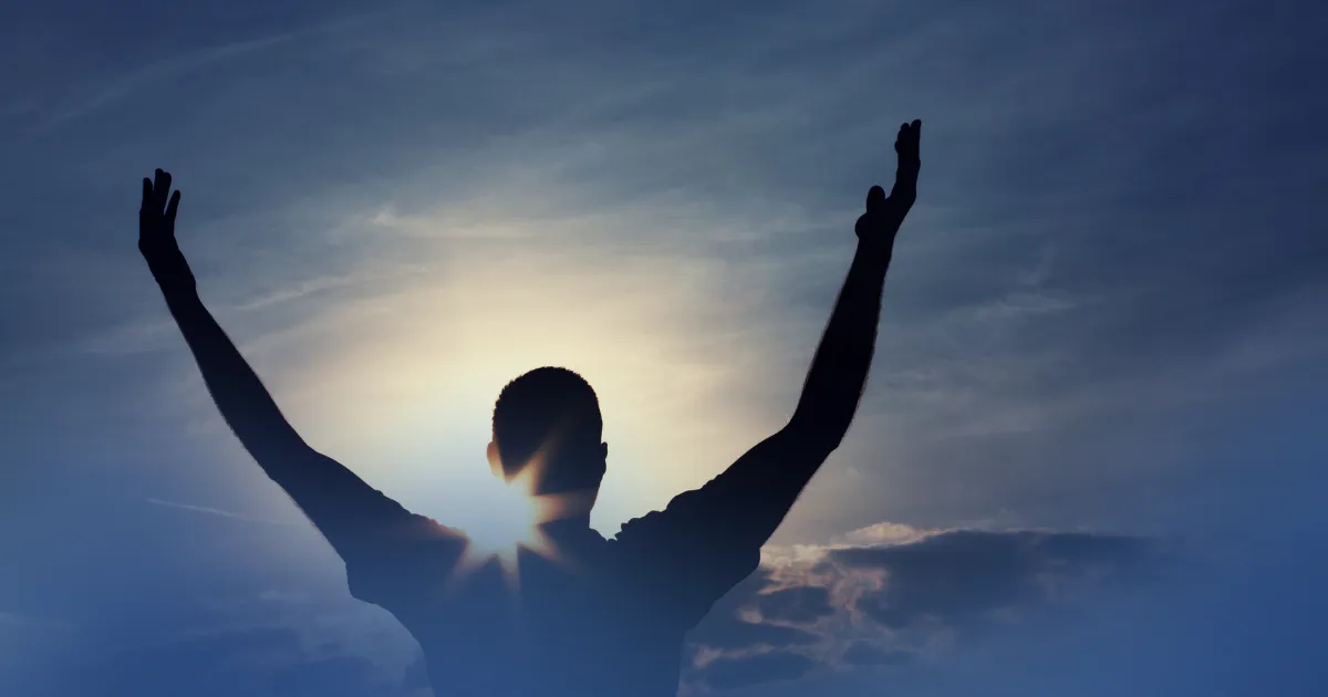 Silhouette of athlete looking up toward bright sunlight breaking through clouds, symbolizing faith, strength, and spiritual connection in sports performance