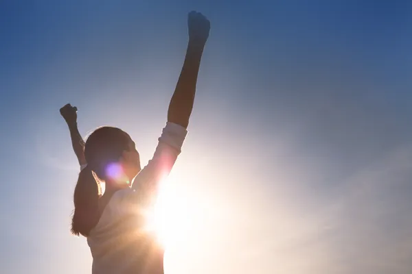 Female athlete with mental strength has her hands up in the sky symbolizing triumphing over adversity