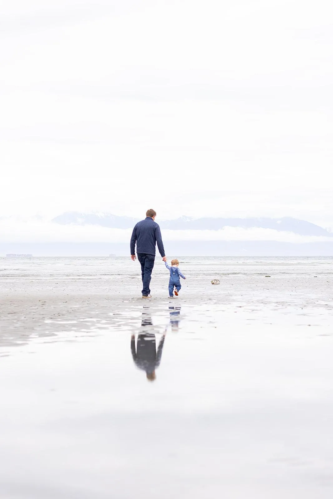 Dad and son walk hand-in-hand on Witty's Beach in Metchosin BC