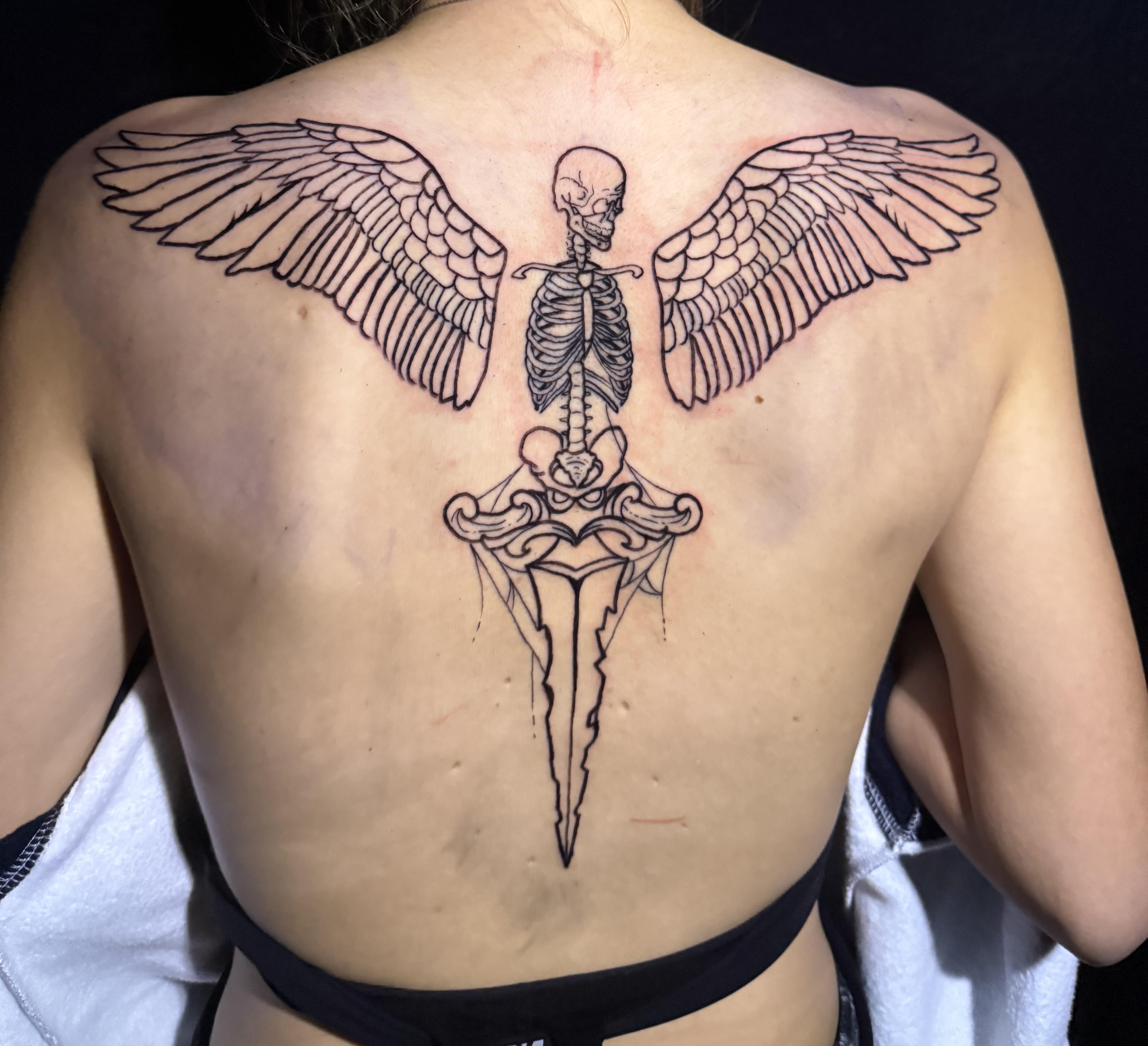 Photo of client's back with a skeleton dagger and wings tattoo by Aiden at Red Arbor Tattoo