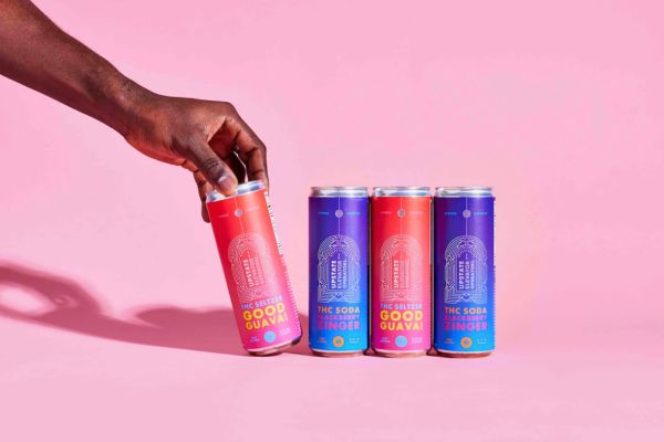 Hand holding a cannabis-infused seltzer can next to assorted THC beverage cans