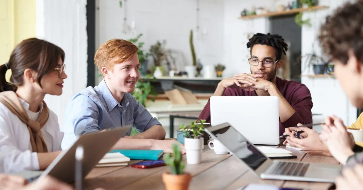 Group of diverse young professionals having a discussion around a table with laptops and notebooks, representing a collaborative workplace environment—ideal for illustrating topics on probationary employees and HR practices.