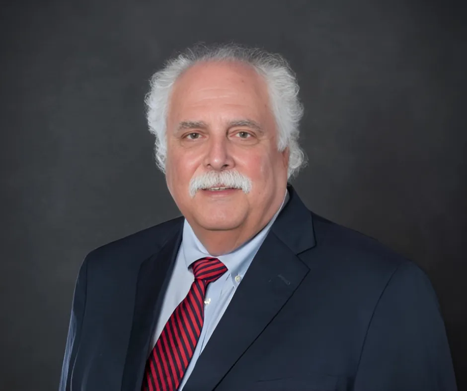 Portrait of Andrew James Paterno, CEO of Centurion Insurance, wearing a dark suit, light blue shirt, and red striped tie, against a dark background.