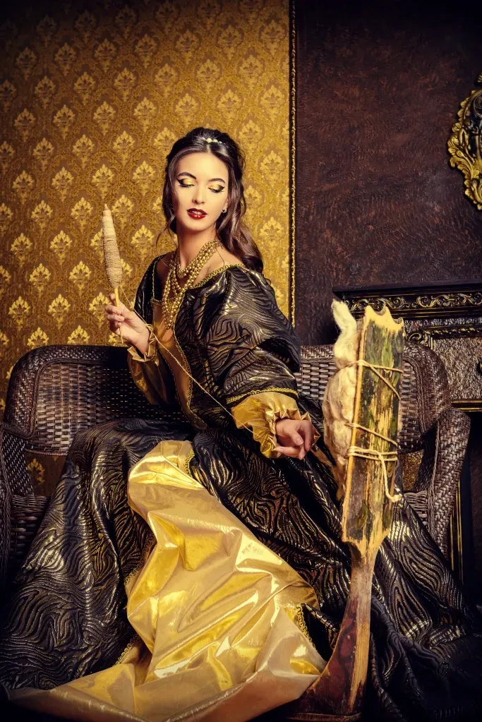 An ancient woman with long hair is wearing a gold gown and pulling wool