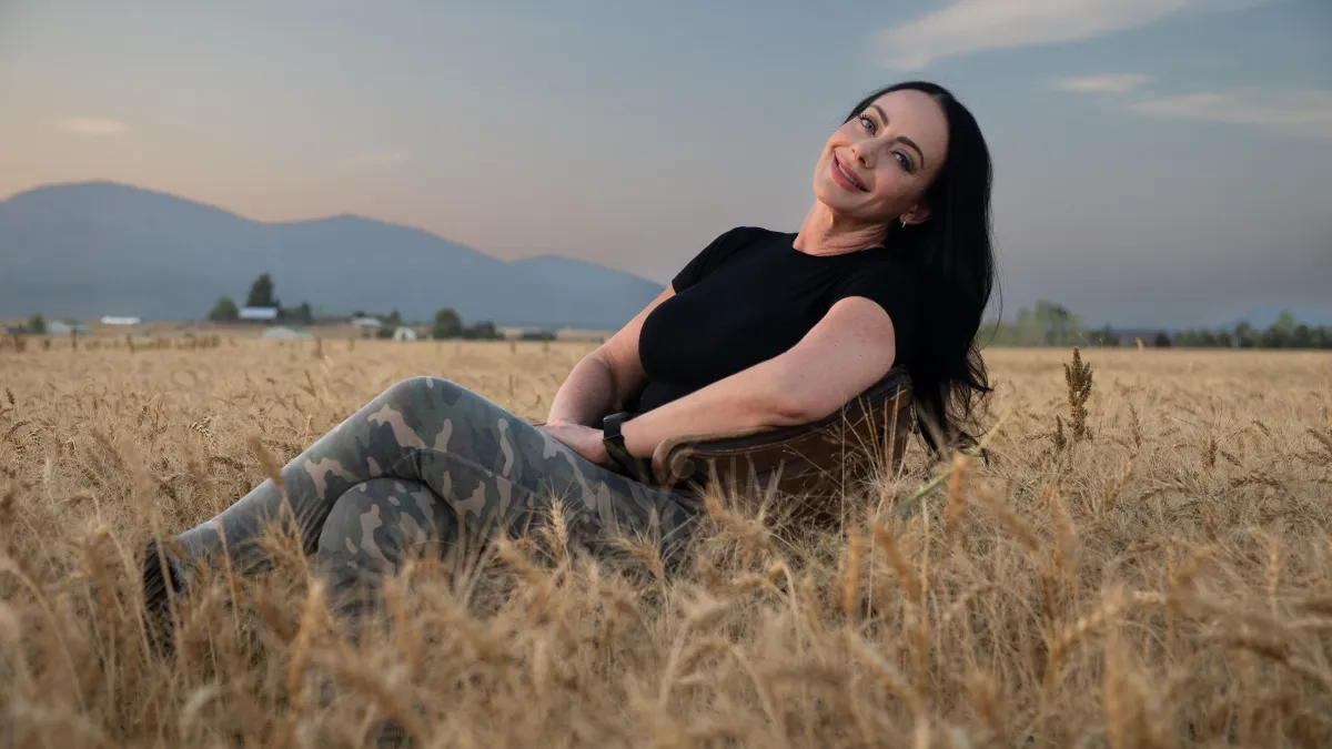Jen Sells sitting in a wheat field at sunset, smiling and relaxed, lifestyle photo for Boss Life Journal blog.