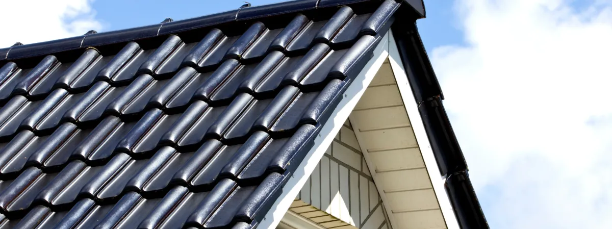 Close-up view of a modern, sleek black tile roof on a residential home against a clear blue sky. Highlighting durability, aesthetic appeal, and energy efficiency, ideal for homeowners exploring roofing solutions.