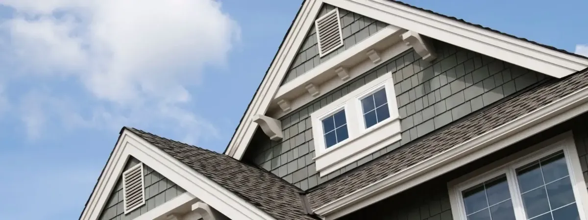 A close-up view of a residential roof and upper exterior siding on a sunny day, showcasing well-maintained shingles and proper roof ventilation—highlighting the importance of summer roof care.