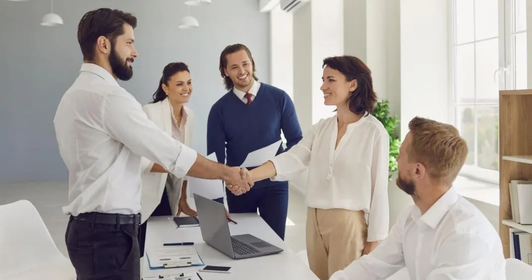 A business owner shaking hands with a new employee during a team meeting, symbolizing successful hiring and positive workplace culture in a service business.