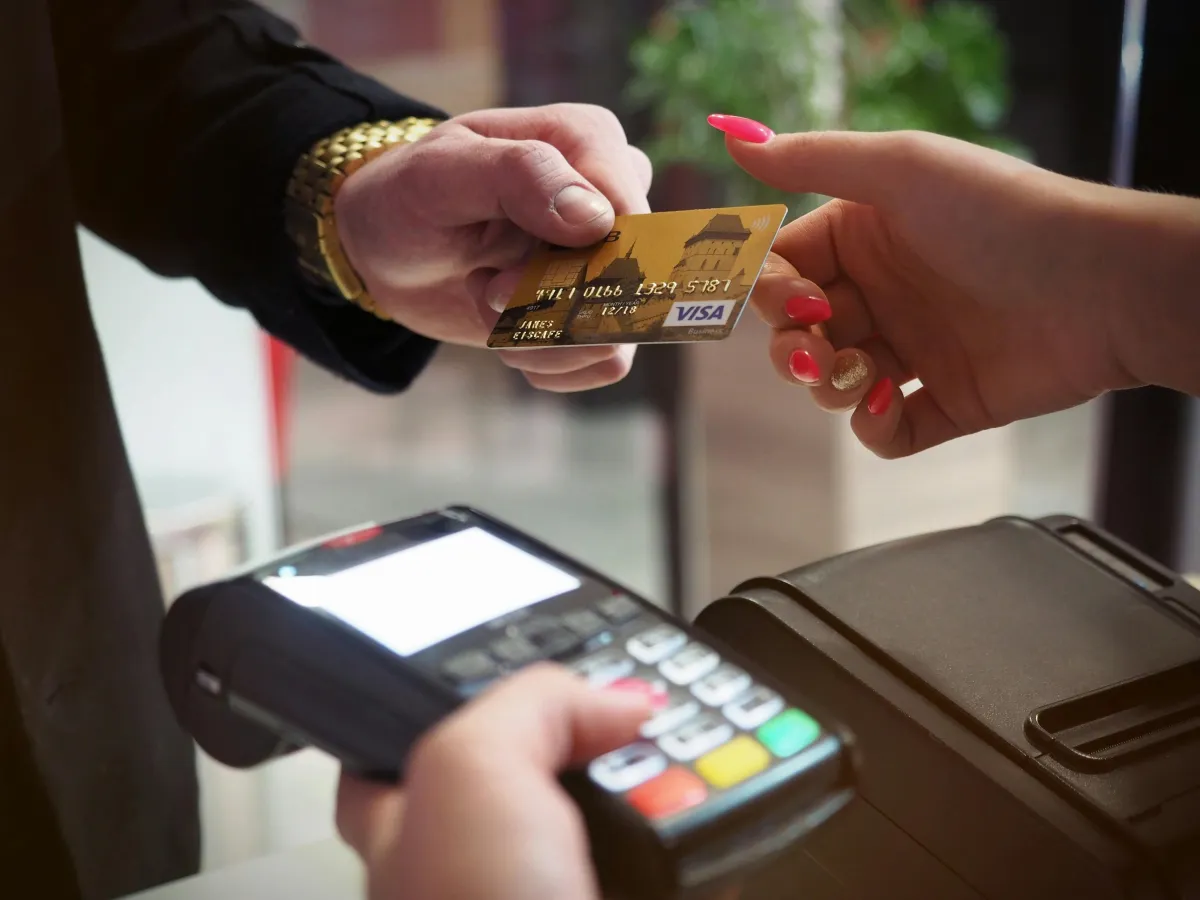 Customer handing a Visa credit card to a merchant using a modern payment terminal at a store counter, showcasing seamless credit card payment processing with MerchaMax Payment Processing.