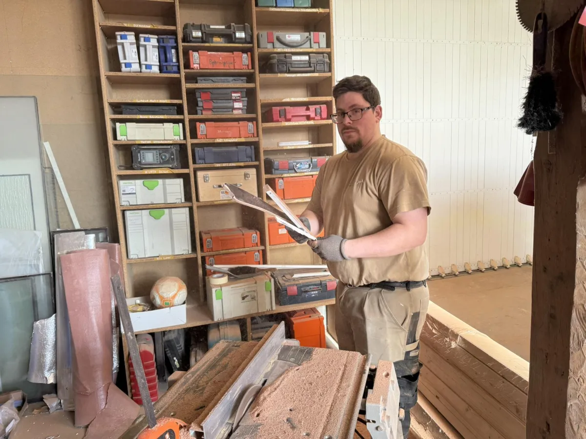 Handwerker in einer Tischlerei arbeitet mit Holz, umgeben von Werkzeugen und Materialien