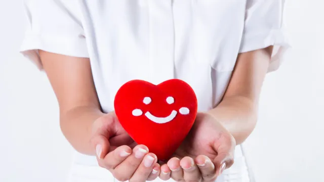 A nurse in a white uniform gently holds a smiling red heart, symbolizing the passion for nursing that should be focused on studying for the NCLEX, not just the application paperwork.