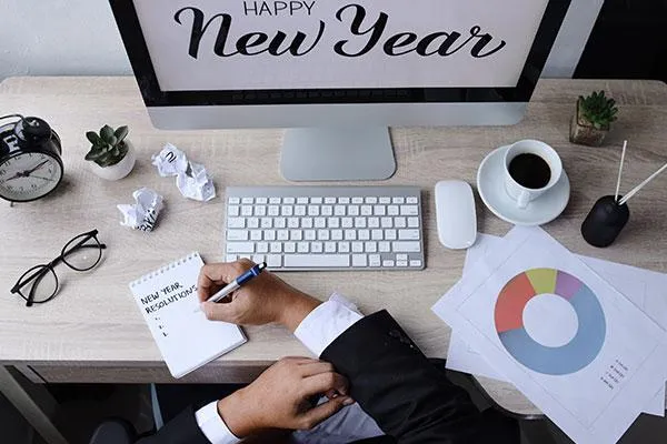 Hand writing New Year Resolution with a monitor displaying Happy New Year in the background, symbolizing SME goals for 2025.
