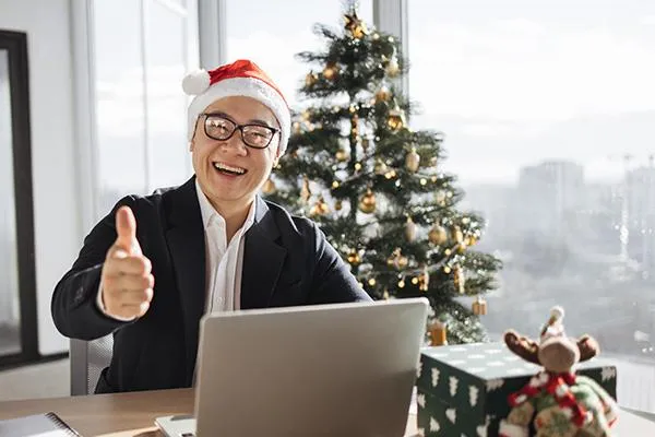 Manager giving a thumbs-up behind a laptop, with a Christmas tree and cityscape in the background, symbolizing SME health benefits readiness for 2025