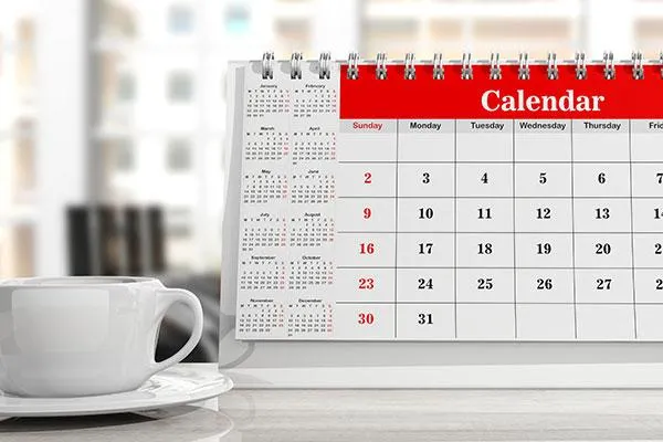 A desk calendar displaying a monthly view with a cup of coffee beside it