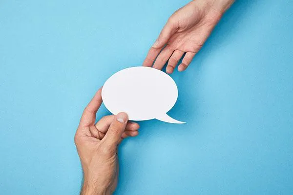 Two hands exchanging a blank speech bubble cutout against a blue background