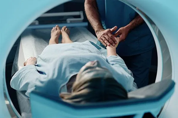 A patient lying on an MRI machine while a healthcare professional holds their hand