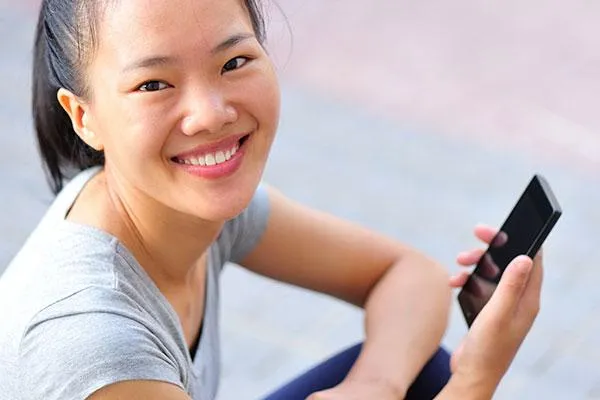 A smiling woman in a casual outfit holds a smartphone