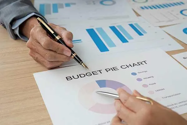 Two people reviewing financial reports and a budget pie chart on a desk, symbolizing SME budget planning for employee health benefits.