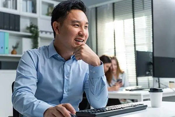 A smiling man in a blue shirt working at his office computer, symbolizing confident HR planning and preparation for the new year.