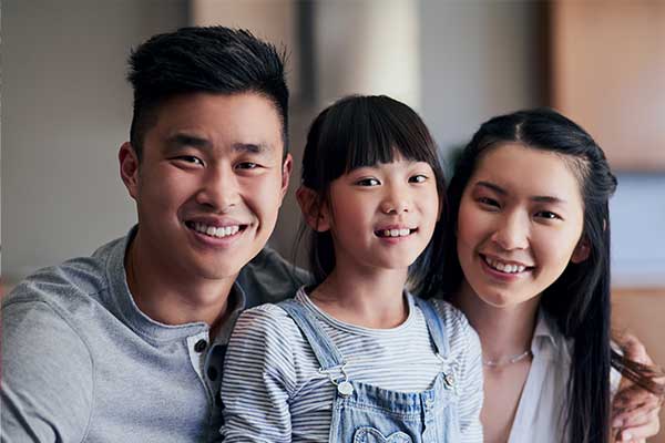 A smiling family with two parents and a young child sitting closely together indoors.