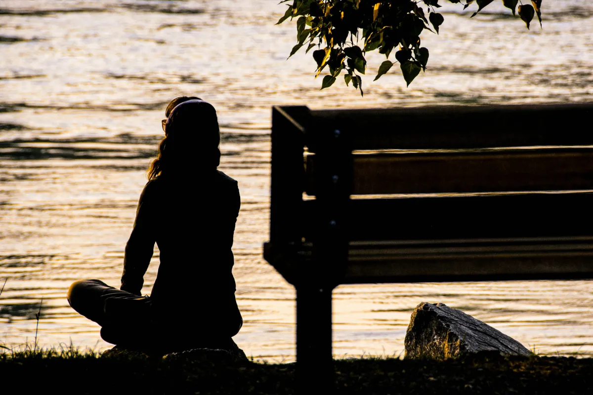 A woman sitting beside the water in meditation and contentment at sunset