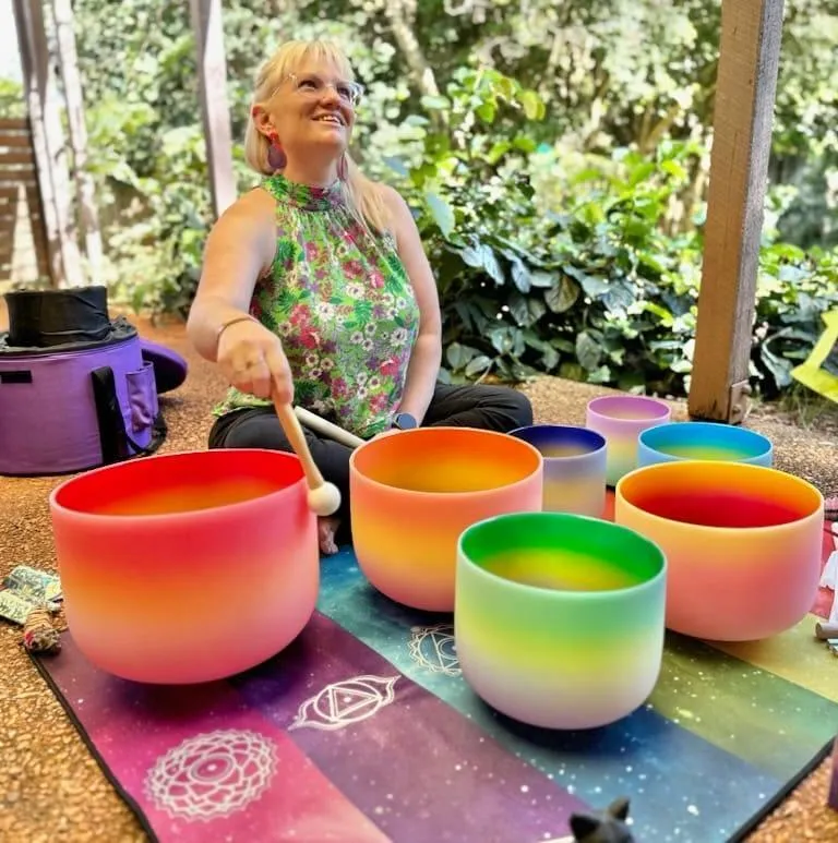 Female Sitting With Rainbow Coloured Sound Healing Crystal Bowls
