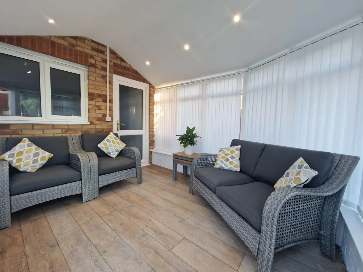 A beautifully designed conservatory lounge with soft lighting, comfortable rattan furniture, and elegant vertical blinds, creating a warm and inviting space.