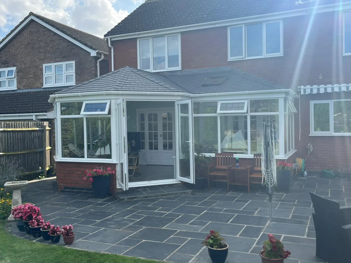A beautifully renovated conservatory with a modern tiled roof and a Velux window, enhancing natural light and energy efficiency. The open doors create a seamless transition between indoor and outdoor living spaces.